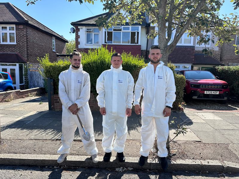 Three Apex crew members in white overalls outside a house